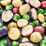 raw potatoes and brussels sprouts on a baking sheet