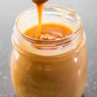 a spoon taking a scoop of caramel sauce from a jar