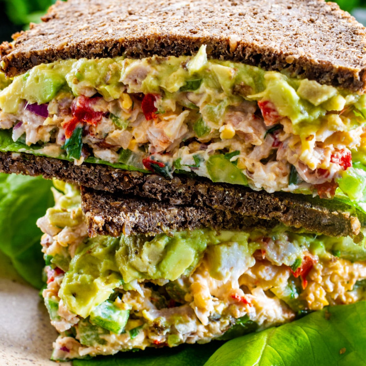 an avocado chicken salad sandwich cut in half and stacked, with the centers exposed