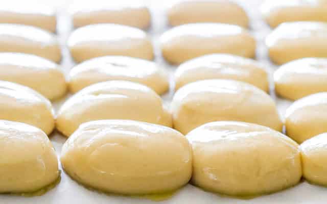 a bunch of slider buns on a baking sheet brushed with butter ready for baking