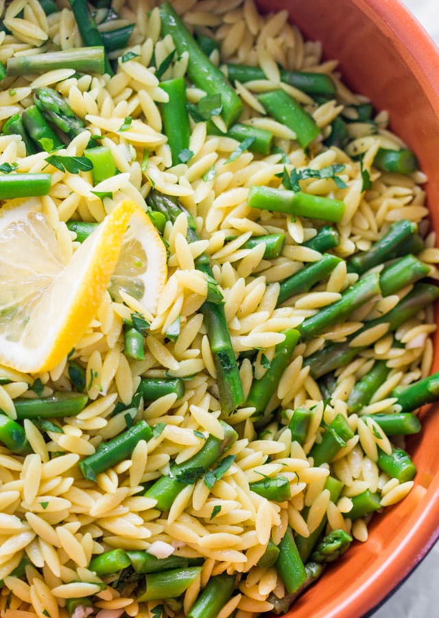 lemon orzo and asparagus in a bowl garnished with a lemon slice