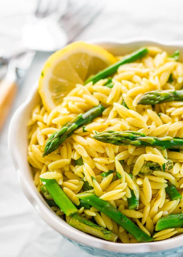 lemon orzo and asparagus in a blue bowl garnished with a lemon wedge
