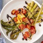 a serving of roasted asparagus and tomatoes with a drizzle of balsamic reduction on a white plate.