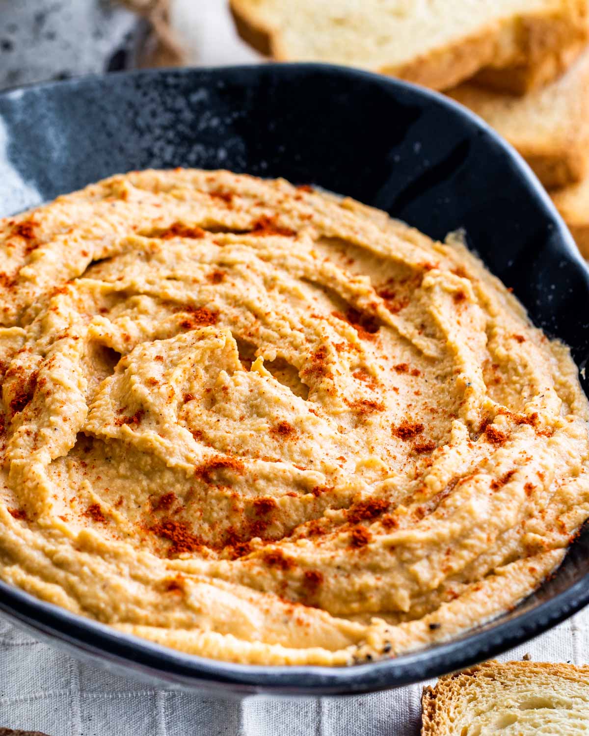 red lentil hummus in a big black bowl garnished with a bit of smoked paprika.