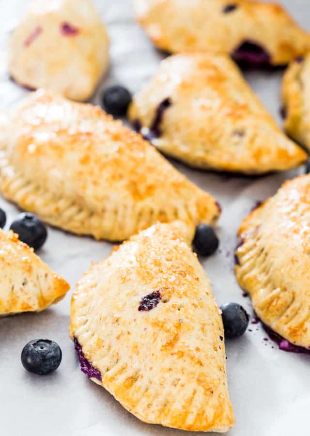 a bunch of blueberry empanadas on fresh out of the oven on parchment papger