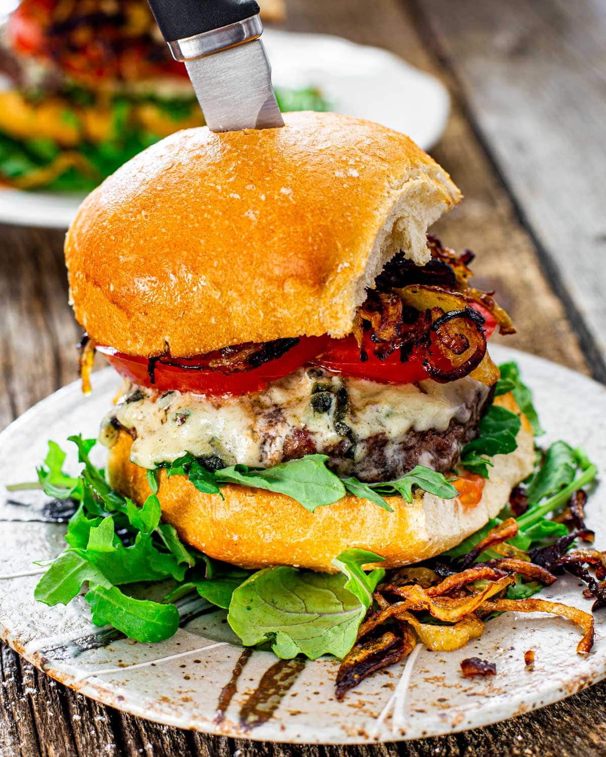 a gorgeous blue cheese burger with crispy fried onion on a plate with a knife in it