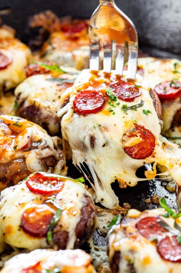 a fork picking up a pizza stuffed mushroom from a skillet full of them