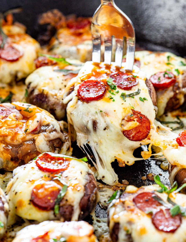 a fork picking up a pizza stuffed mushroom from a skillet full of them