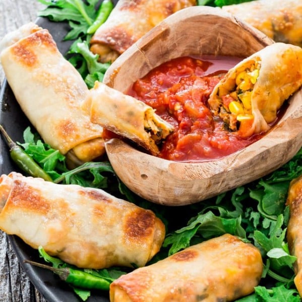 spicy baked mexican egg rolls surrounding a bowl of salsa on a plate