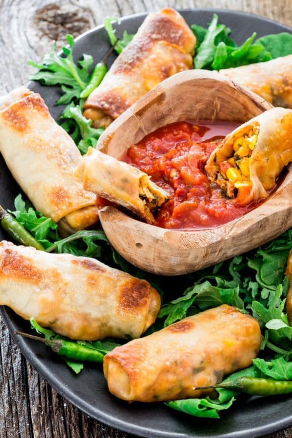 spicy baked mexican egg rolls surrounding a bowl of salsa on a plate