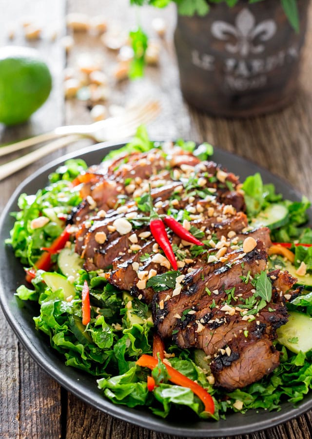 thai steak salad on a black platter garnished with red thai chilis