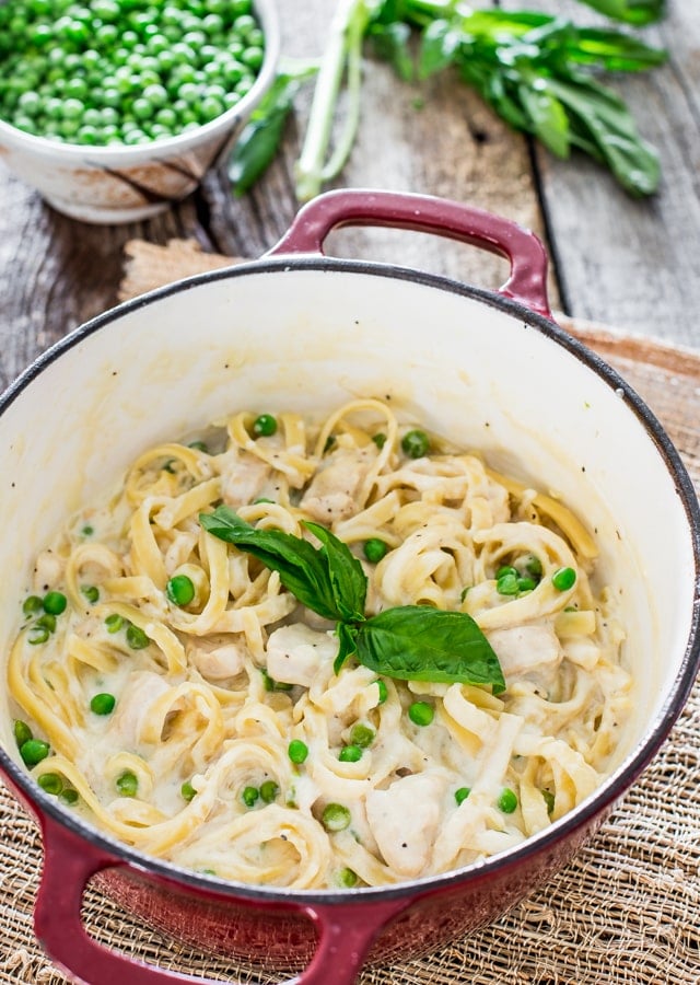 a dutch oven filled with fettuccine alfredo with chicken and peas