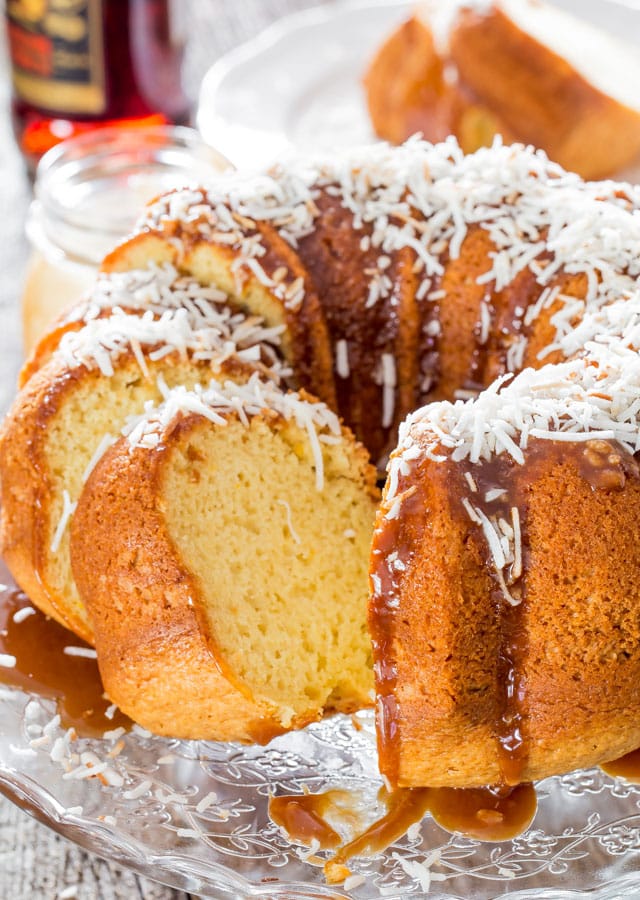 bermuda rum cake sliced on a cake platter, topped with shredded coconut and caramel rum sauce