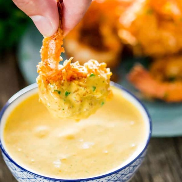 a hand dipping a coconut shrimp into the spicy mango dipping sauce