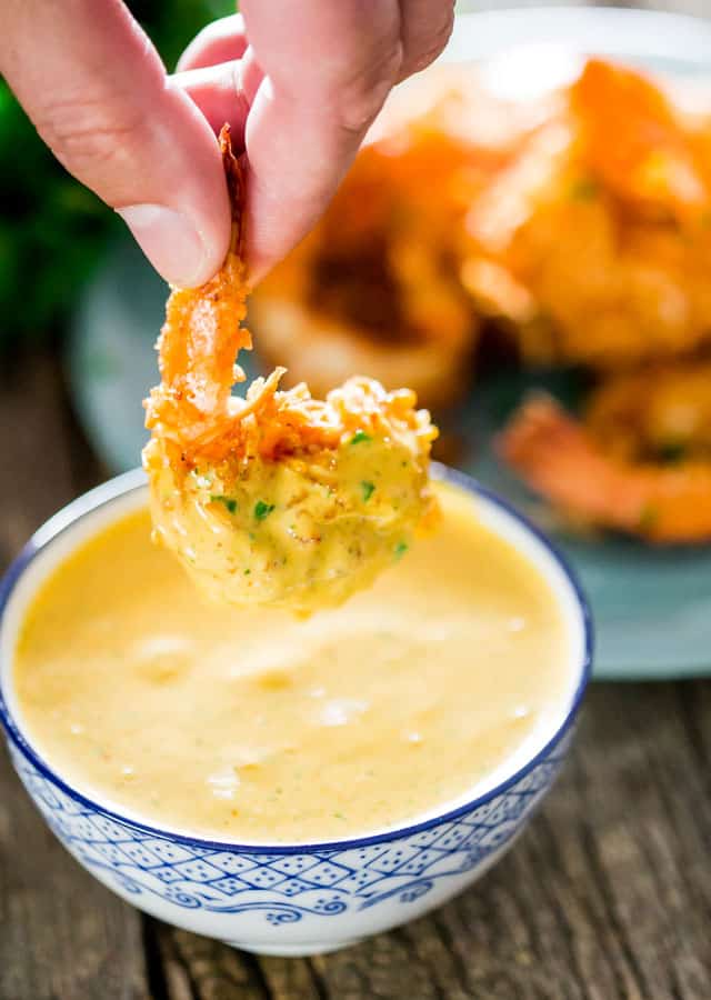 a hand dipping a coconut shrimp into the spicy mango dipping sauce
