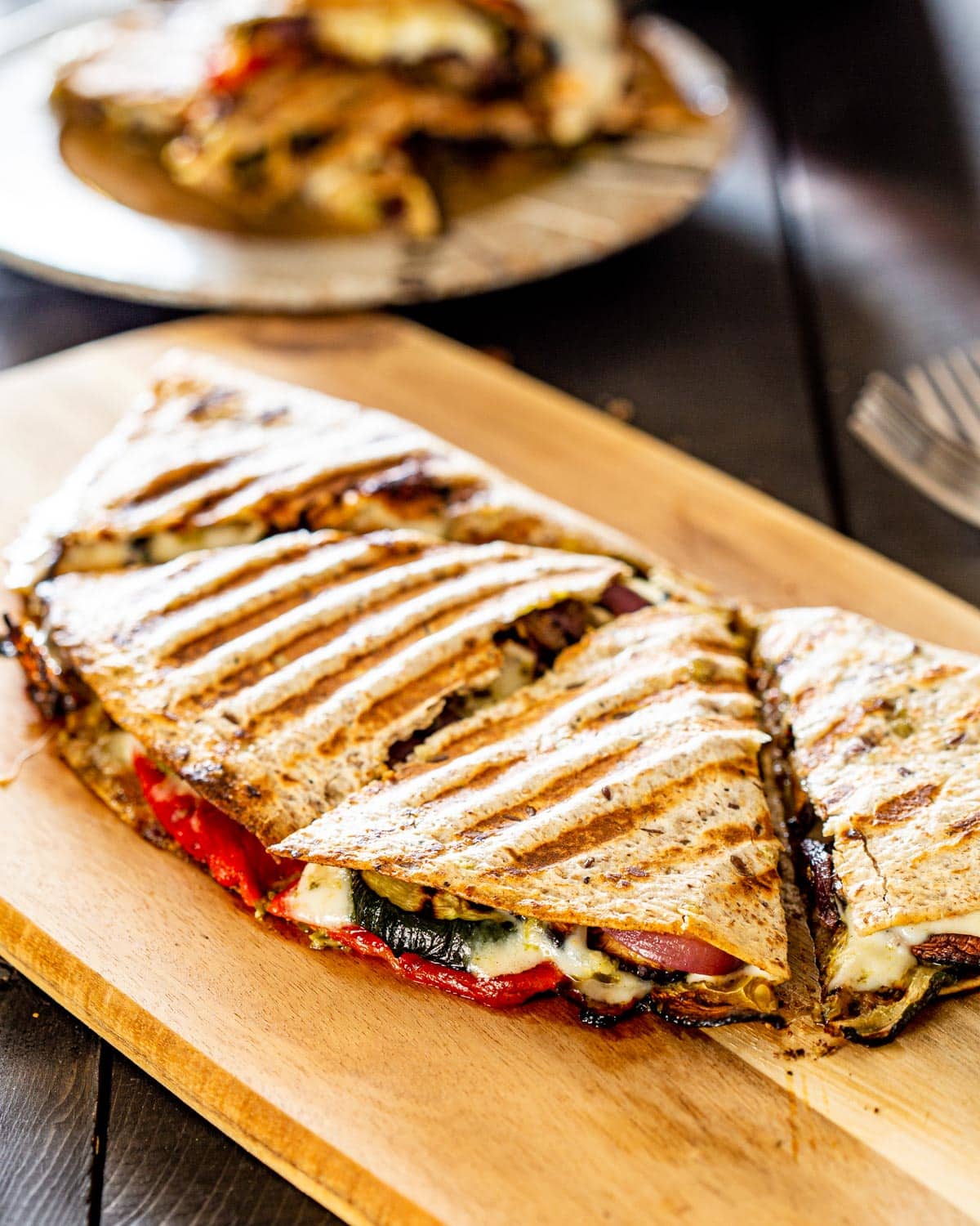 a grilled vegetable quesadillas on a cutting board cut in quarters with a plate in the background