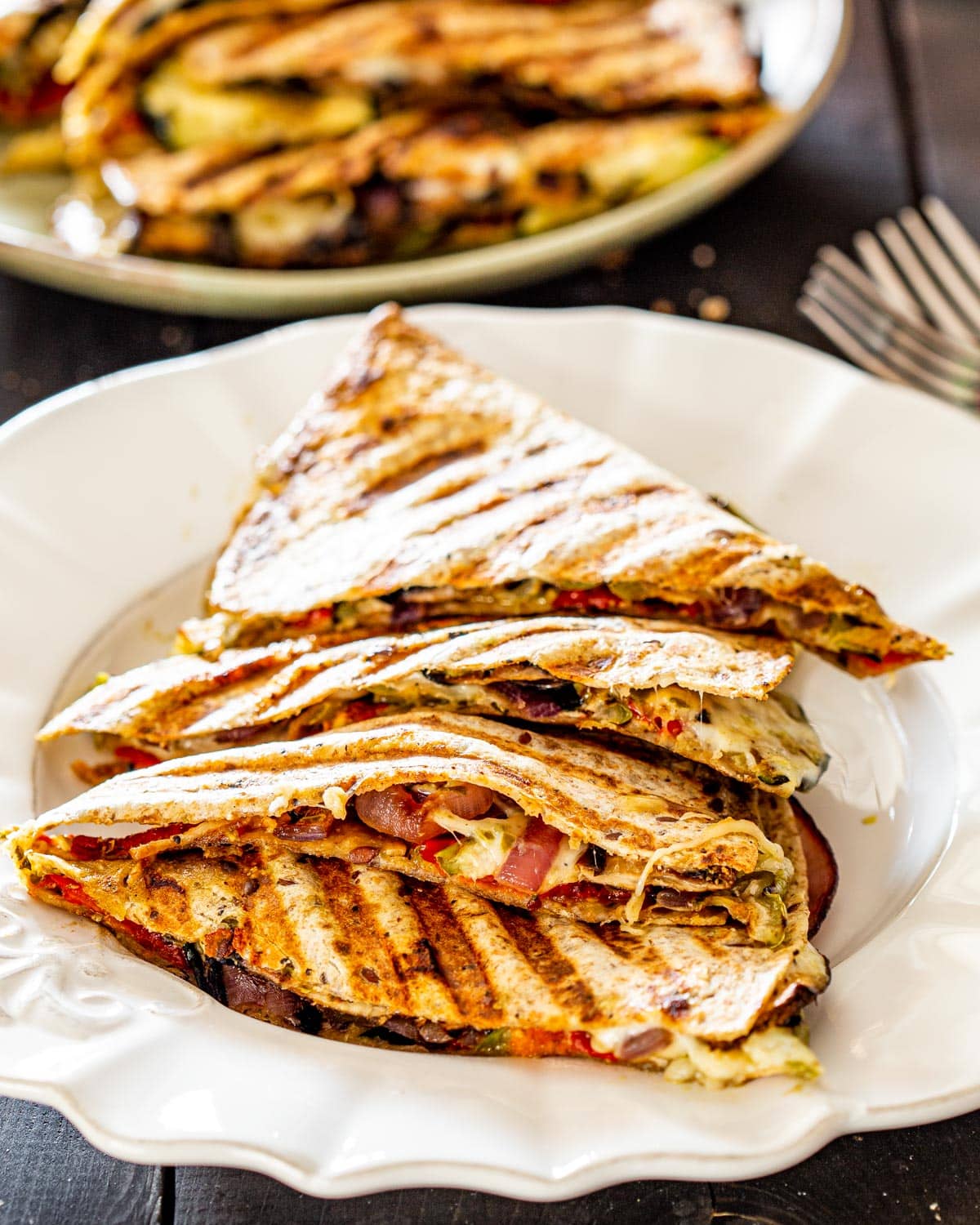 a white plate with a stack of grilled veggie quesadillas with another plate in the background