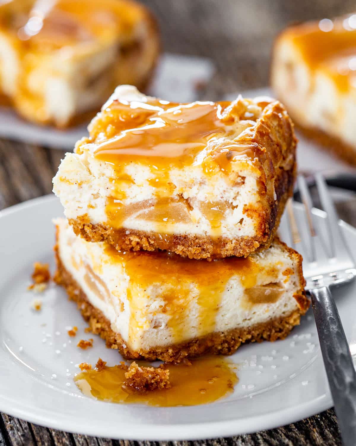 2 apple pie cheesecake bars stacked on top of each other topped with caramel sauce