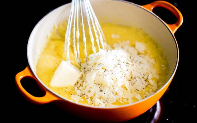 making polenta with butter and parmesan cheese in an orange dutch oven