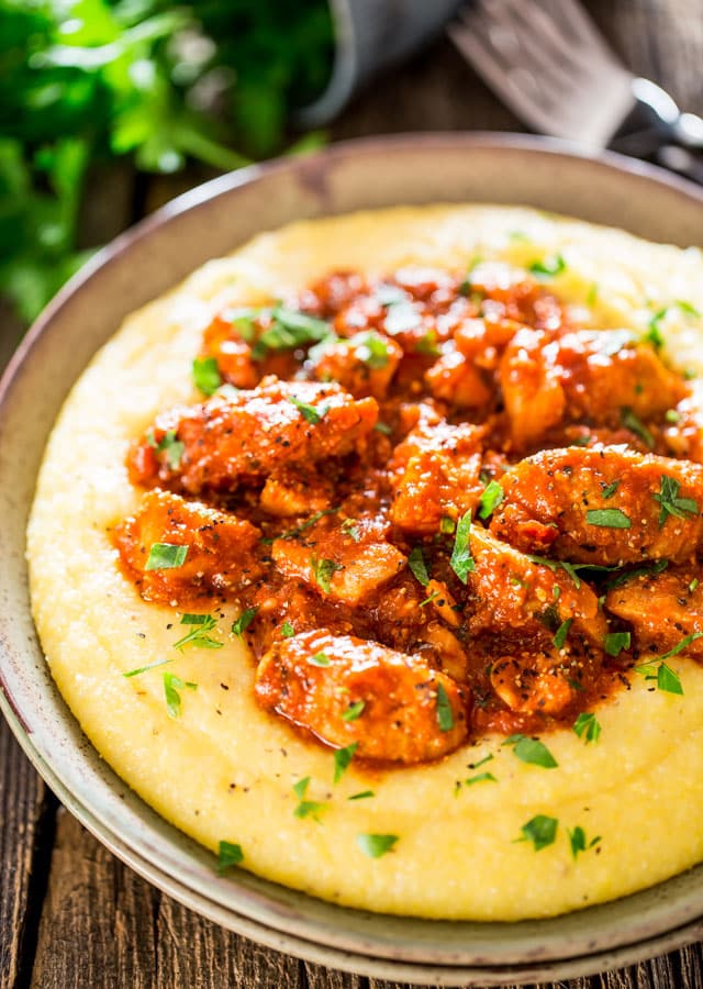 Saucy Chicken and Sausage over Creamy Parmesan Polenta  on a plate garnished with parsley