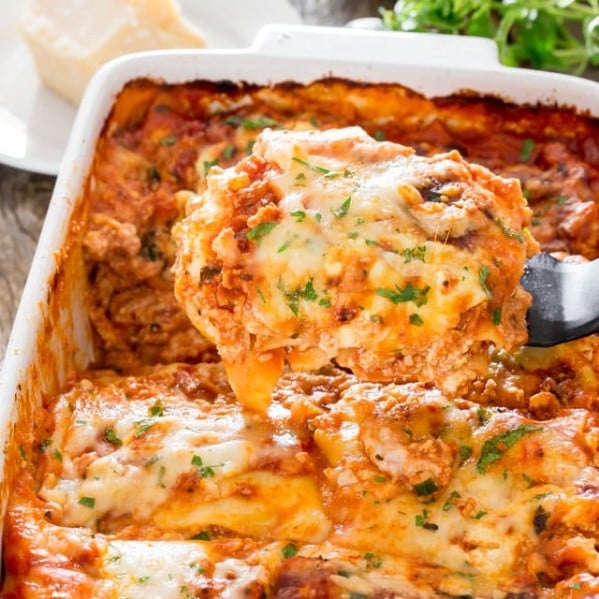 a spatula lifting a piece of chicken bolognese lasagna from the baking dish