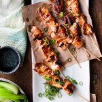 chinese chicken skewers on a plate topped with green onions