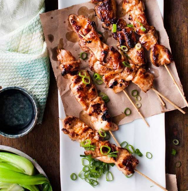 chinese chicken skewers on a plate topped with green onions
