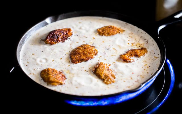 cooked chicken thighs in a creamy sauce being cooked with orzo in a skillet