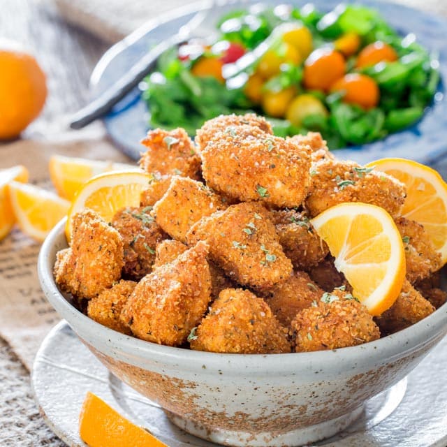 closeup of chicken milanese in a bowl garnished with lemon wedges