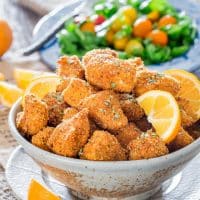 a bowl full of chicken milanese bites garnished with orange wedges