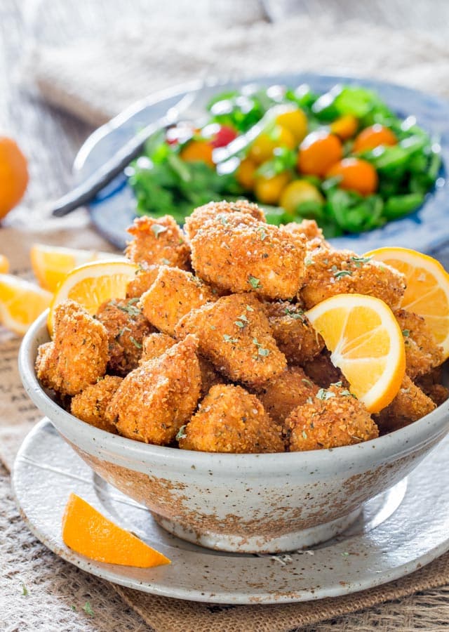 chicken milanese bites in a bowl garnished with lemon wedges and a salad in the background