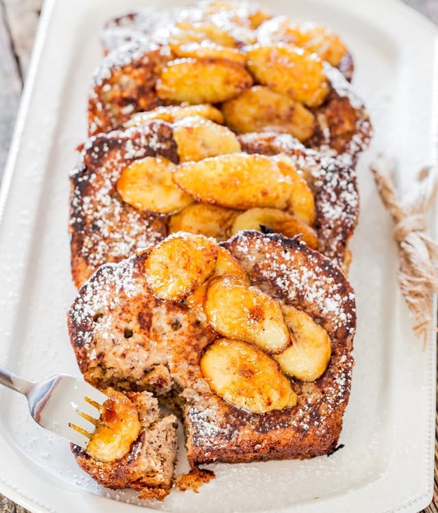 a fork taking a bite of banana bread french toast with caramelized bananas on a plate