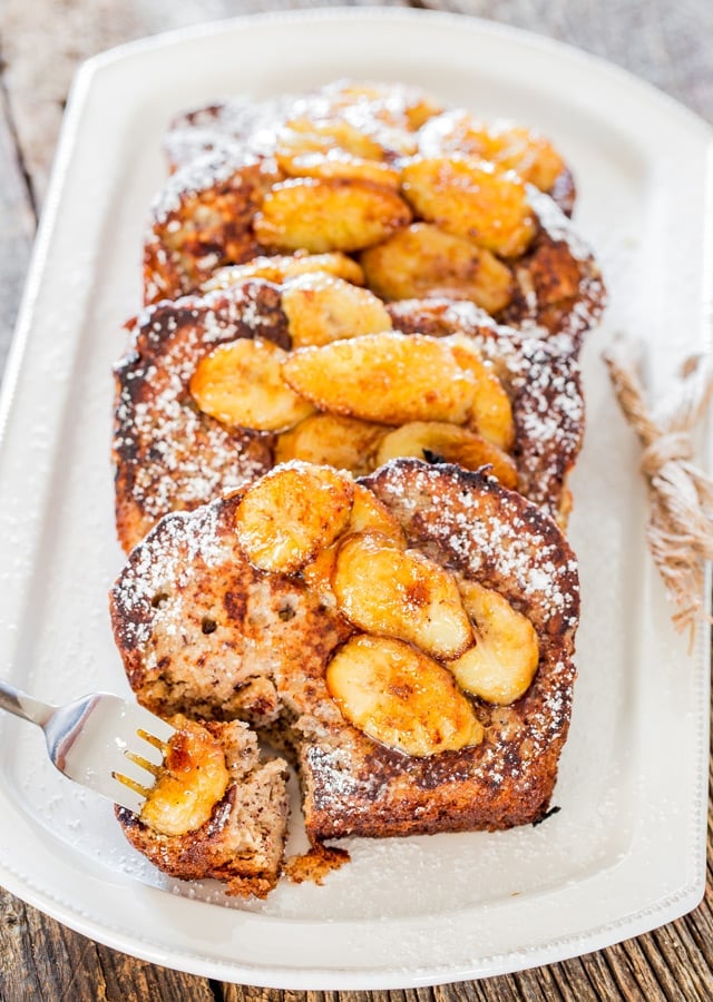 a fork taking a bite of banana bread french toast with caramelized bananas on a plate