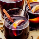 two glasses of mulled wine with oranges and cinnamon sticks
