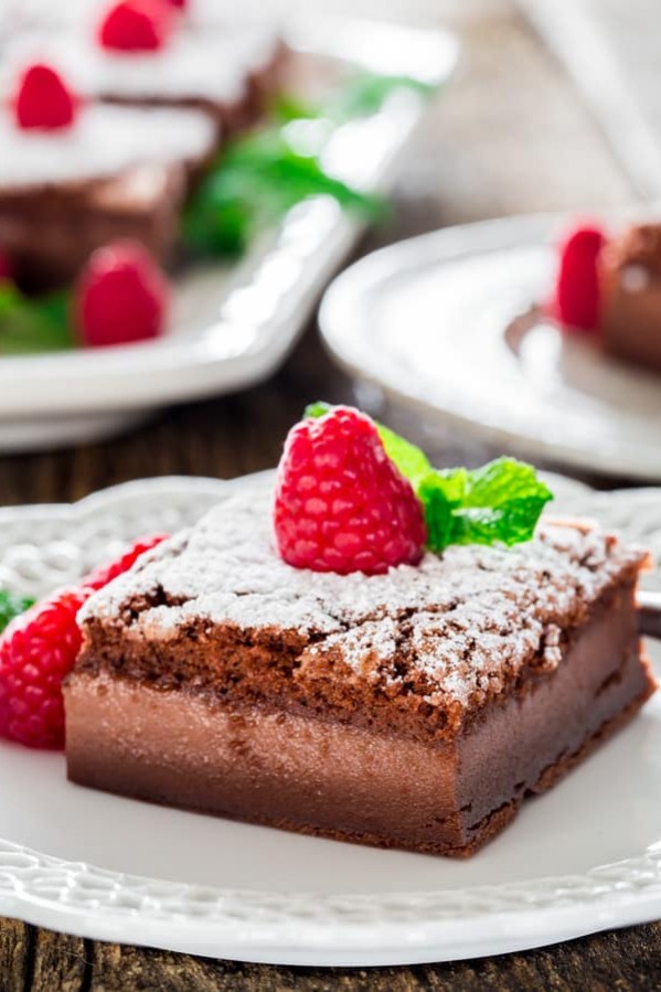 a slice nutella magic cake dusted with powdered sugar and topped with a fresh raspberry on a plate