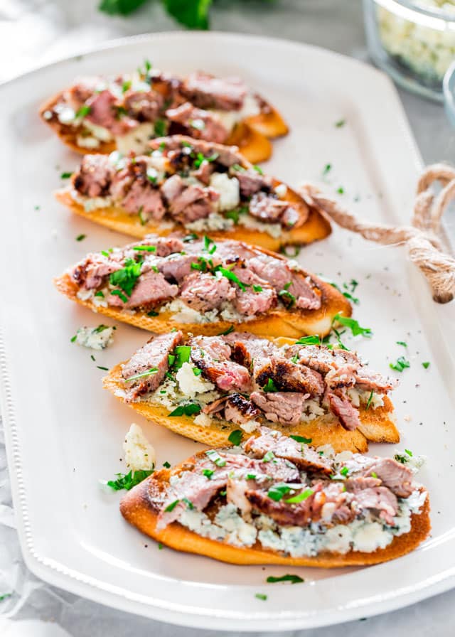 5 Blue Cheese and Steak Crostini lined up on a platter