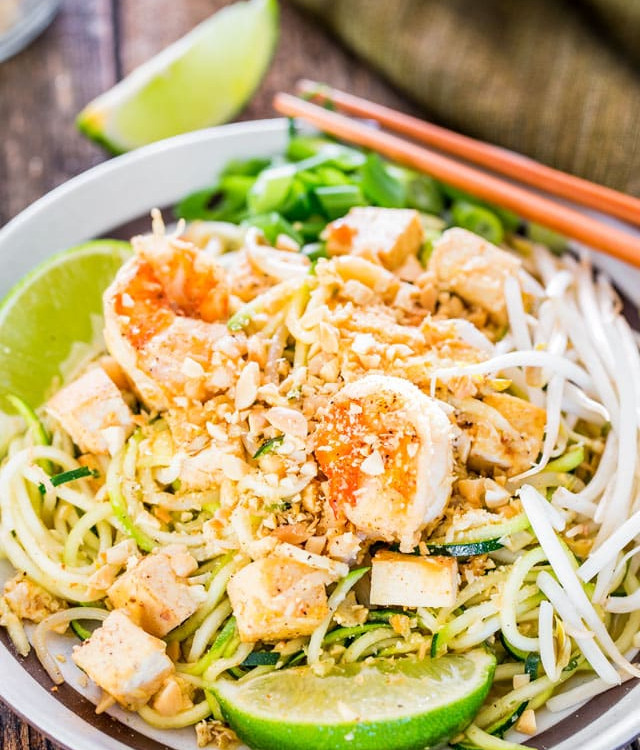 a plate of pad thai zoodles garnished with lime wedges
