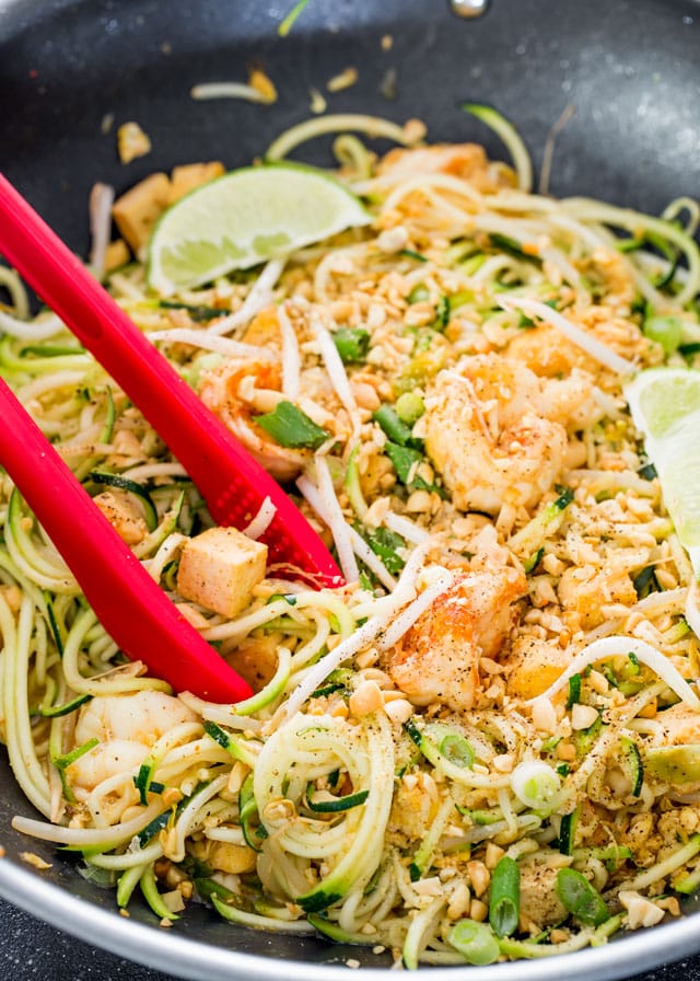 Pad Thai Zoodles in a wok with lime wedges and tongs