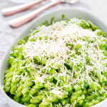 a bowl of arugula and walnut pesto pasta topped with shredded parmesan cheese