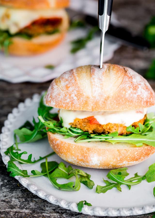 a Chicken Parmwich on a plate with arugula and a knife through it