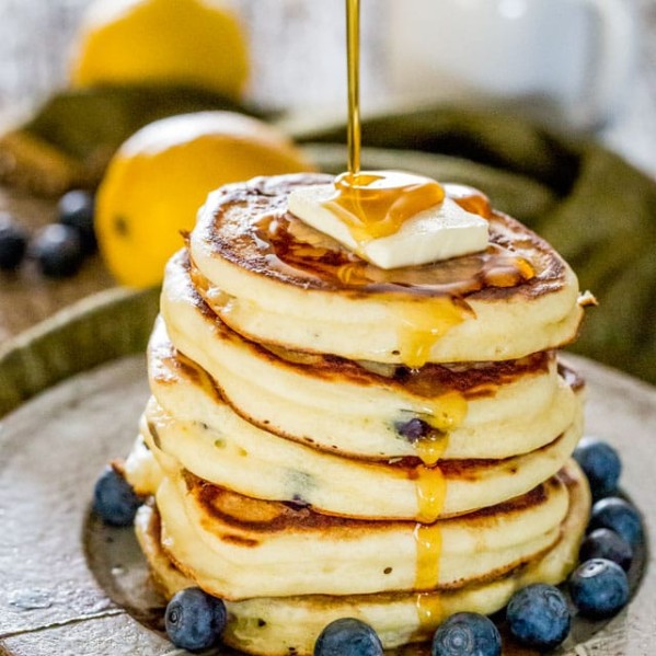 side view shot of maple syrup being drizzled over a stack of pancakes