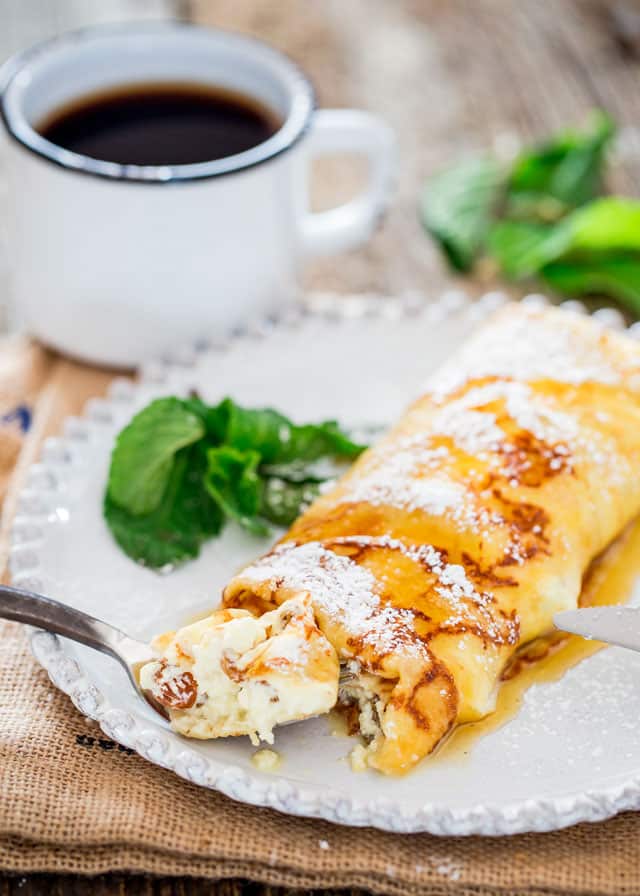 Maple Ricotta Stuffed Crepes on a plate with a fork and a cup of coffee