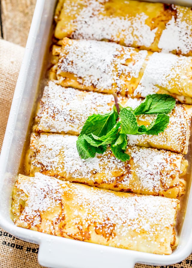 Maple Ricotta Stuffed Crepes in a casserole dish topped with icing sugar and a sprig of mint