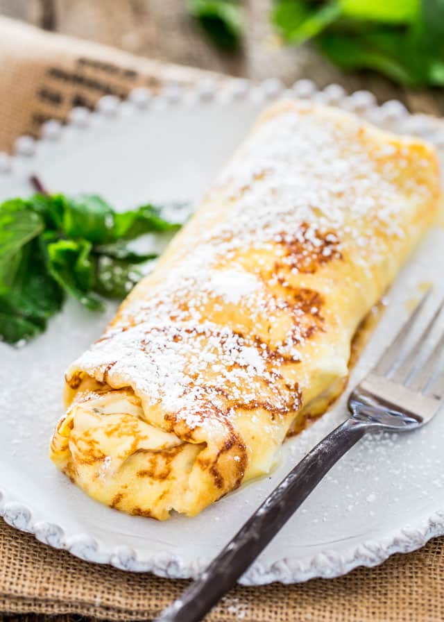 Maple Ricotta Stuffed Crepes on a plate topped with icing sugar
