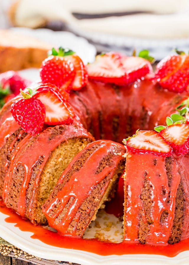 a pound cake with a slice cut out covered in glaze and topped with fresh strawberries