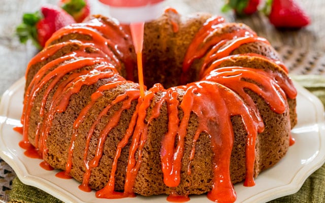 a pound cake being drizzled with strawberry glaze