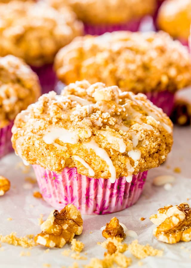 Coffee Cake Muffins drizzled with glaze on parchment paper surrounded by walnuts