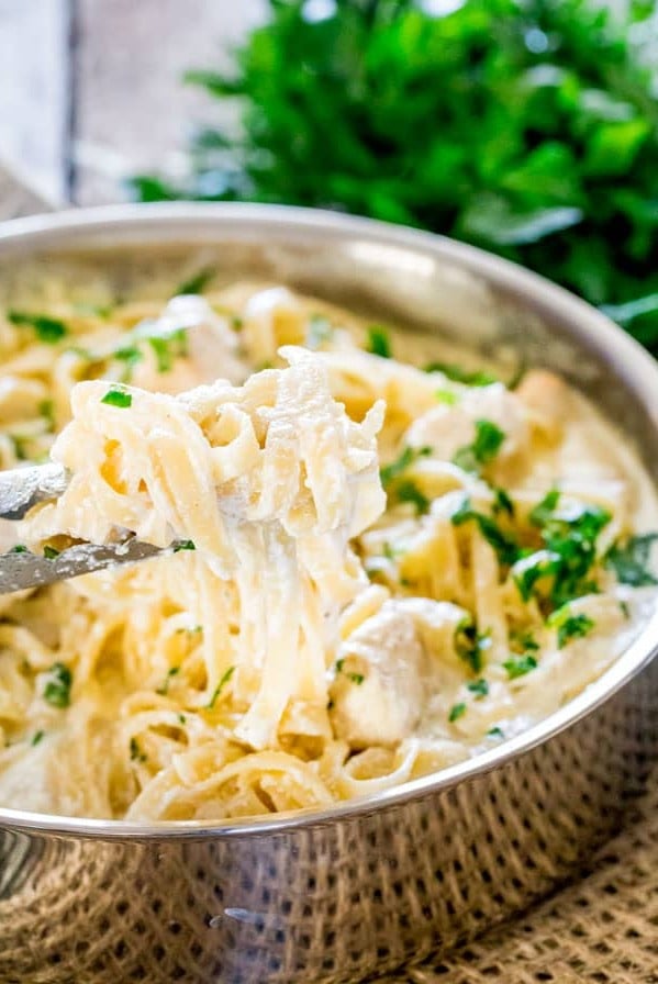 side view shot of tongs holding up chicken fettuccine alfredo