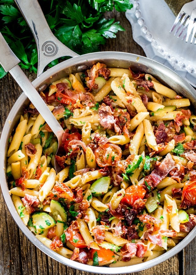 overhead shot of a serving spoon resting in a pot of penne with prosciutto tomatoes and zucchini
