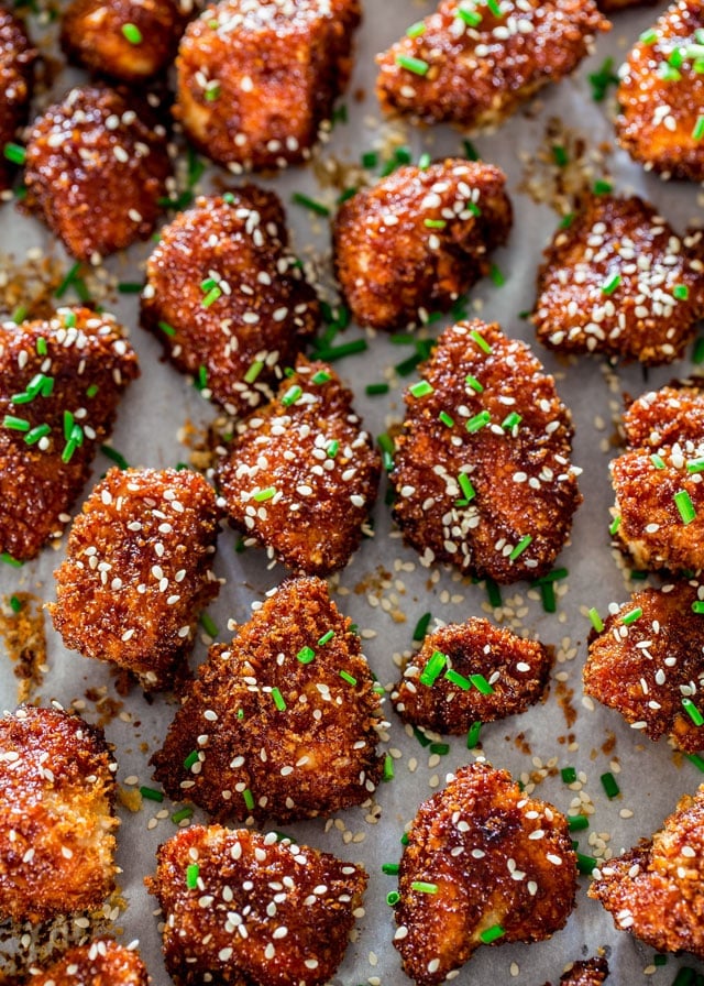 Honey Sriracha Chicken Bites on parchment paper topped with sesame seeds and chives